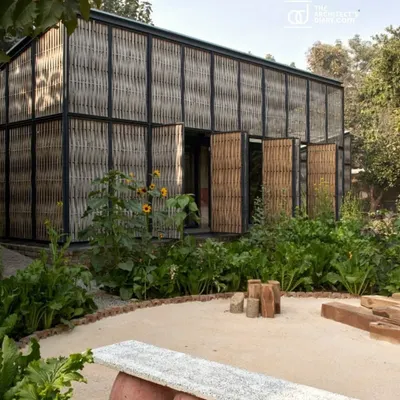 The Artist Residency at Farm8, nestled in a lush green landscape. The structure's facade is a screen of woven bamboo set within a steel frame, creating a porous skin that breathes and allows the building to merge with its organic surroundings.