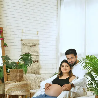 A relaxed and casual maternity portrait of a couple in a bright, bohemian-style studio setting. This image captures their comfortable intimacy and excitement.