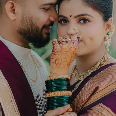 A close-up portrait focusing on the bride's intricate henna and traditional Maharashtrian jewelry. The way she holds her hand near her face draws attention to the beautiful nath and her expressive eyes, creating an intimate and culturally rich image.