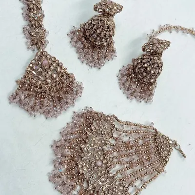 A beautiful mehndi jewelry set in a dusty pink shade. The set includes a maang tikka, jhumkas, and a hathphool, all adorned with delicate beads.