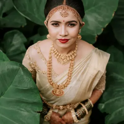 A striking bridal portrait where the bride, in her traditional gold and cream saree, is framed by lush green leaves. We use natural elements to create artistic and memorable portraits that highlight the bride's elegance and personality.