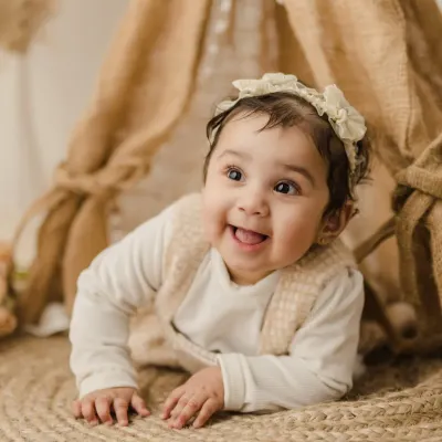 A beautiful shot of a baby girl during her sitter session, crawling on a soft jute rug with an inquisitive and happy expression.