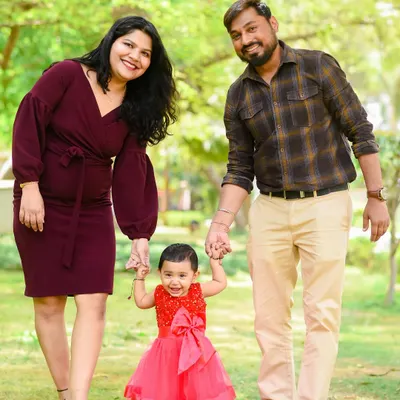 A perfect family portrait. Mom and dad hold their daughter's hands as she takes her first steps, a beautiful memory from her birthday shoot.