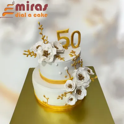 A stunning two-tier cake for a golden 50th birthday. The elegant white and gold design is adorned with beautiful, handcrafted white and gold sugar flowers, creating a sophisticated and memorable centerpiece.