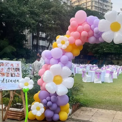 This is another view of our daisy-themed outdoor balloon arch. This angle shows how the arch integrates with the event space, alongside a welcome easel displaying photos of the birthday girl, Ariana.