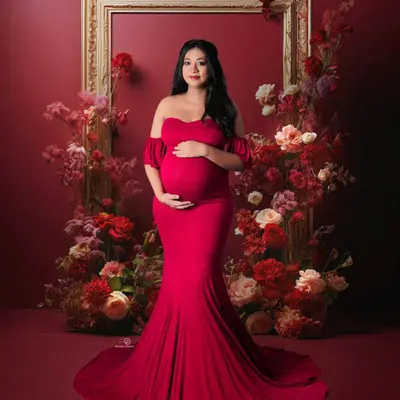 A stunning studio portrait featuring a gorgeous mom-to-be in a classic red off-shoulder gown. The floral frame adds a touch of romance and artistry to this elegant maternity photo.