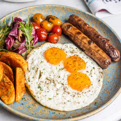 A classic breakfast plate featuring sunny-side-up eggs with perfectly runny yolks, paired with savory sausages, potato wedges, and a side of fresh greens. This is the kind of meal that fuels your entire day.