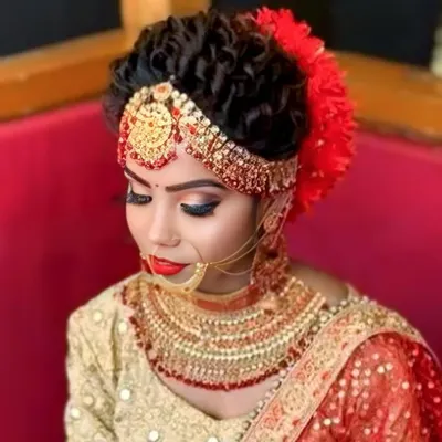A classic North Indian bridal updo with tight curls, a matha patti, and bold red floral accessories. You'll learn how to create a strong foundation for heavy jewelry and dupattas.