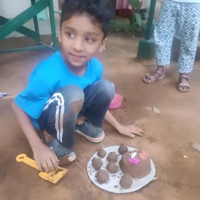 A young boy proudly displays his mud cake creation. This sensory activity allows children to explore textures and shapes using natural materials.