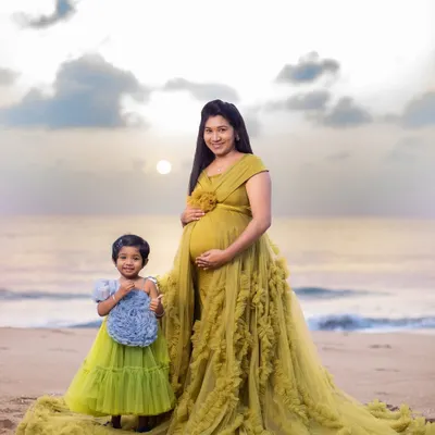 A portrait of a mother and daughter against the soft morning sky. The coordinated flowing gowns add a touch of elegance to this beautiful beach maternity photo, celebrating the bond they share before the new baby arrives.