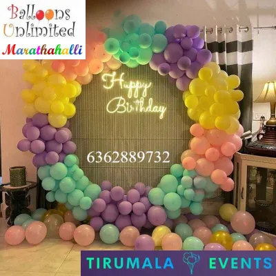 A beautiful pastel rainbow balloon ring with a 'Happy Birthday' neon sign, creating a perfect photo corner in a home.