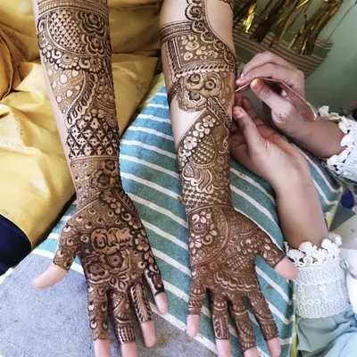 A moment from a mehendi session, showing the application process. You can see the name 'Salman' being intricately woven into the palm, and the half-finished design on the other arm.