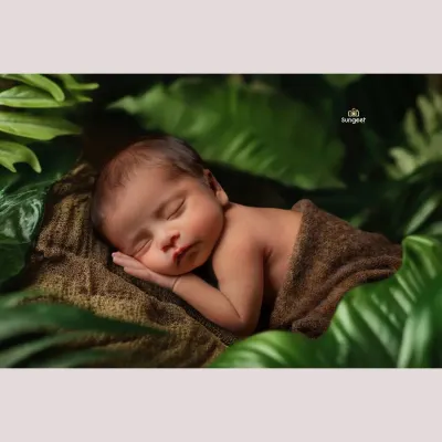 Tucked away in a lush, green world of his own. This nature-inspired newborn shot uses soft textures and deep greens to create a peaceful, organic feel, highlighting the baby's serene expression.