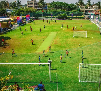 A wide-angle view of a busy training day at our academy. Multiple groups of young athletes engage in various football drills across the expansive green field, showcasing the energy and scale of our program.