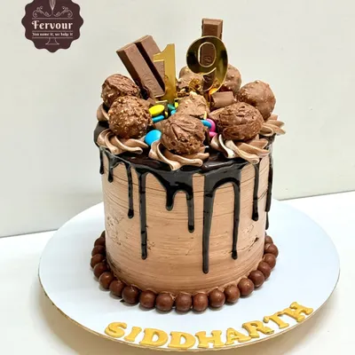 A chocolate overloaded cake for a 19th birthday. This tall drip cake is covered in chocolate frosting and topped with Ferrero Rocher, KitKats, and Gems.