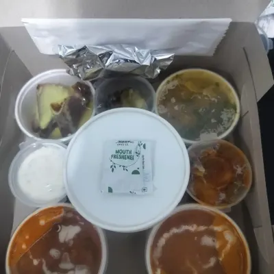 An overhead view of our executive meal box. This thali-style packaging includes multiple curries, raita, dessert, and a mouth freshener, ensuring a complete and satisfying lunch.