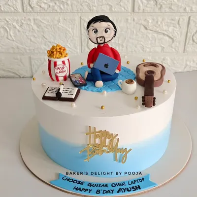 A fully customized cake for Ayush, featuring all his favorite things. The handcrafted fondant toppers include him with his laptop, a guitar, popcorn, a book, and his phone, with a fun message to "Choose Guitar Over Laptop."