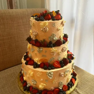 This 10kg, three-tiered vanilla sponge cake was infused with orange zest and decorated with Swiss meringue buttercream, fresh berries, and palette knife flowers for a grand celebration.