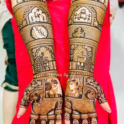 A complete bridal story. This design features beautiful Raja-Rani portraits on the palms, couple initials, and traditional motifs like peacocks and elephants, telling a full love story on the bride's hands.