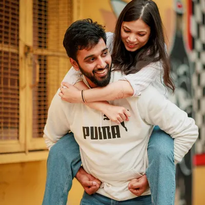 A fun and spontaneous piggyback moment from a casual pre-wedding shoot in Delhi. This image perfectly captures the playful and carefree dynamic of the couple against a vibrant, artistic city wall.