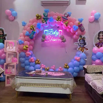 A beautiful Kanha ji themed baby shower, perfect for a divine blessing. This setup features a circular balloon arch in pink and blue, a glowing neon "Baby Shower" sign, and cutouts of Radha and Krishna.