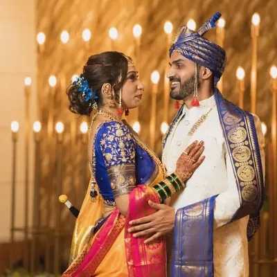 A royal portrait of a Maharashtrian couple in stunning traditional attire, with the groom in a royal blue turban and the bride in a vibrant Paithani saree.