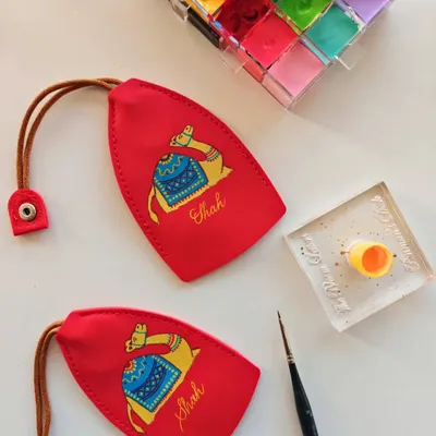 The details are what I love most. Here, I'm hand painting a colorful camel illustration and adding the family name 'Shah' to a bright red leather keychain, creating a vibrant and personal accessory.