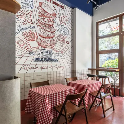 The hero of this diner's interior is the hand-drawn style mural, which we designed to capture the fun and flavor of the brand. It serves as a dynamic backdrop to the dining area, which features classic red-and-white checkered tablecloths.