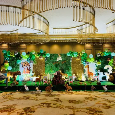 A wide shot of a grand jungle theme stage in a large hall, showing the scale of the setup with multiple animal props and green foliage backdrops.