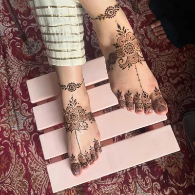 A beautiful and delicate foot mehendi design, featuring a central floral motif with a trailing pattern on the toes and a matching anklet band.