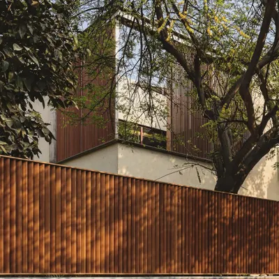 A facade composed of vertical wooden louvers provides privacy and shade while allowing for natural ventilation. This skin gives the building a warm, textured appearance that is rooted in its natural surroundings.