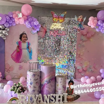 A full view of an enchanting butterfly-themed first birthday. This grand setup includes a double balloon arch in pink, purple, and silver, a central shimmer wall, and a personalized backdrop featuring the birthday girl's photo.