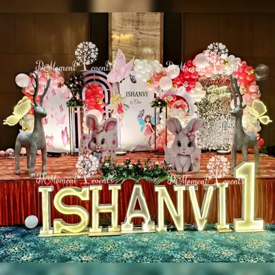A magical first birthday stage combining winter wonderland and fairy themes. The setup features adorable bunny and reindeer props, a sparkling sequin backdrop, and balloon arrangements in festive red and white, creating a whimsical forest scene.