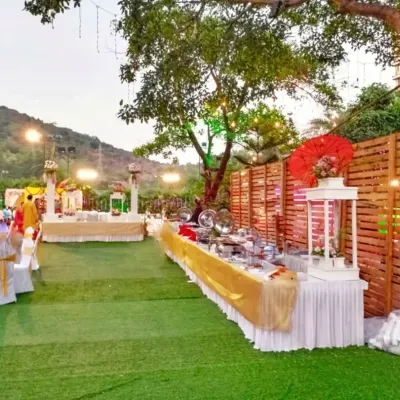 This is an example of an outdoor buffet setup on an artificial lawn. The serving tables are neatly dressed with white and gold fabrics, ensuring the catering area looks organized and inviting for guests.