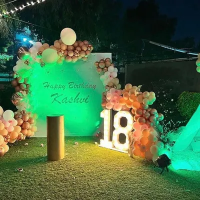 An 18th birthday on a lawn, shown here with green lighting. The setup includes a personalized backdrop and marquee numbers.
