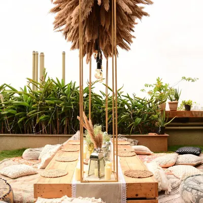 A detailed look at our boho sit-down arrangement. The centerpiece is a tall metal structure filled with pampas grass, with Edison bulbs hanging down to light the low wooden table.