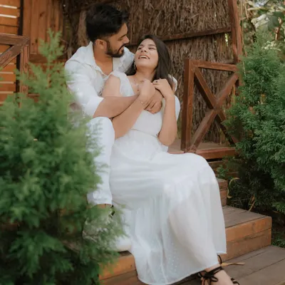 A moment of pure, uninhibited laughter on a rustic wooden porch. Dressed in coordinated white, this couple's joy is infectious, showcasing a perfectly candid moment from their pre-wedding shoot.