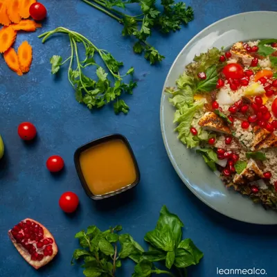 Our Couscous Salad is a perfect, light-yet-filling meal. This top-down view shows the vibrant mix of fluffy couscous, juicy pomegranate seeds, fresh herbs, and grilled chicken, served with a zesty dressing on the side.