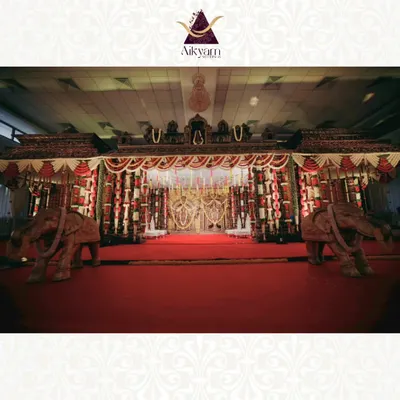 A classic temple-style mandap designed for a grand wedding ceremony. The stage is framed by carved elephants and adorned with traditional red and white floral garlands, creating a regal and sacred space.