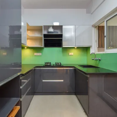 A U-shaped modular kitchen with glossy grey cabinets and a vibrant green backsplash. This design maximizes counter space and storage, with everything easily within reach for an efficient cooking experience.