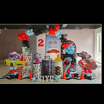 This 'Two Fast' racing theme for Niyaan is ready for the fast lane. The setup includes a checkered flag backdrop, multiple car cutouts, a custom-designed floor mat that looks like a zebra crossing, and a balloon arch that mimics a finish line.