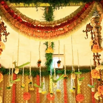 A full view of a traditional backdrop we created for a half-saree function. The design is rich with layers of marigold, jasmine, and tuberose garlands, accented with brass temple bells for an authentic feel.