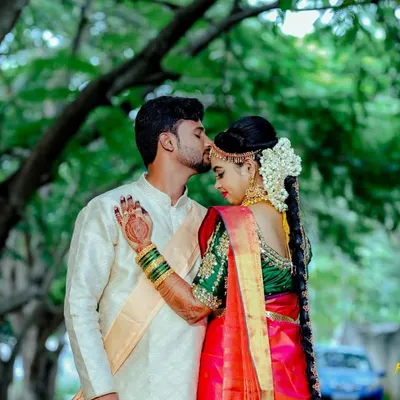 A tender forehead kiss shared between a couple in beautiful traditional attire. The bride's red and green silk saree and the groom's cream sherwani create a classic and elegant look.