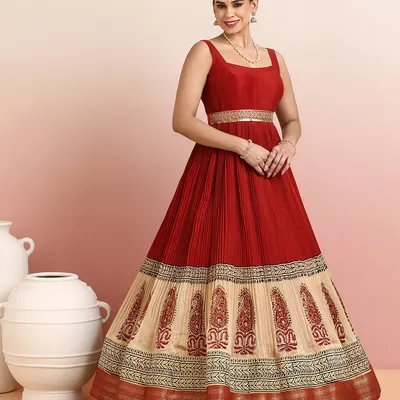 A masterpiece of grace, this regal red and beige gown features a finely pleated bodice and a skirt adorned with ornate paisley embroidery. The shimmering golden zari border adds a touch of heritage charm.
