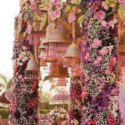 A close-up of the incredible detail from a floral mandap. The pillars are wrapped in thousands of flowers, and ornate, hand-painted bells hang from above, adding a traditional and artistic touch to the Roka ceremony decor.