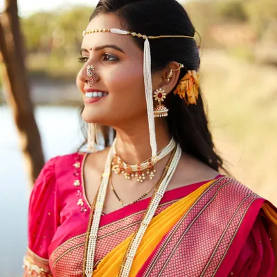 A radiant close-up of a woman in a yellow and pink Nauvari saree, adorned with traditional Maharashtrian bridal jewelry, including the distinctive Mundavalya.