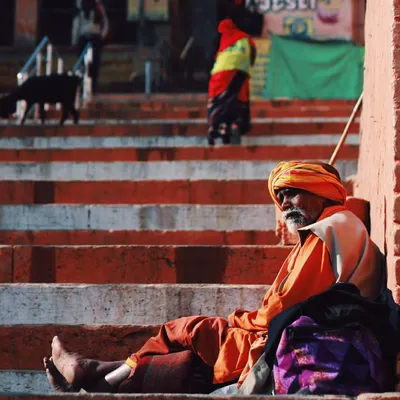 A sadhu rests on the steps of the ghats in Varanasi, his vibrant orange robes contrasting with the weathered stairs. This image captures a moment of peaceful solitude, a common sight in a city that is constantly moving yet full of stillness.