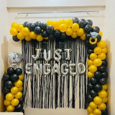 A striking 'Just Engaged' backdrop featuring a black and yellow balloon arch. The metallic silver foil letters stand out against the black fringe, creating a modern and celebratory photo spot.