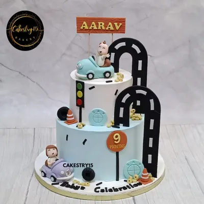 A playful two-tier car-themed cake for a 9-month milestone. This 4kg black forest cake features fondant cars and a winding road design for a fun and adventurous celebration.