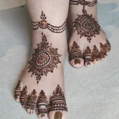 An elegant foot design featuring a central mandala and a delicate chain anklet. The toes are also beautifully decorated, creating a look that is both traditional and chic.